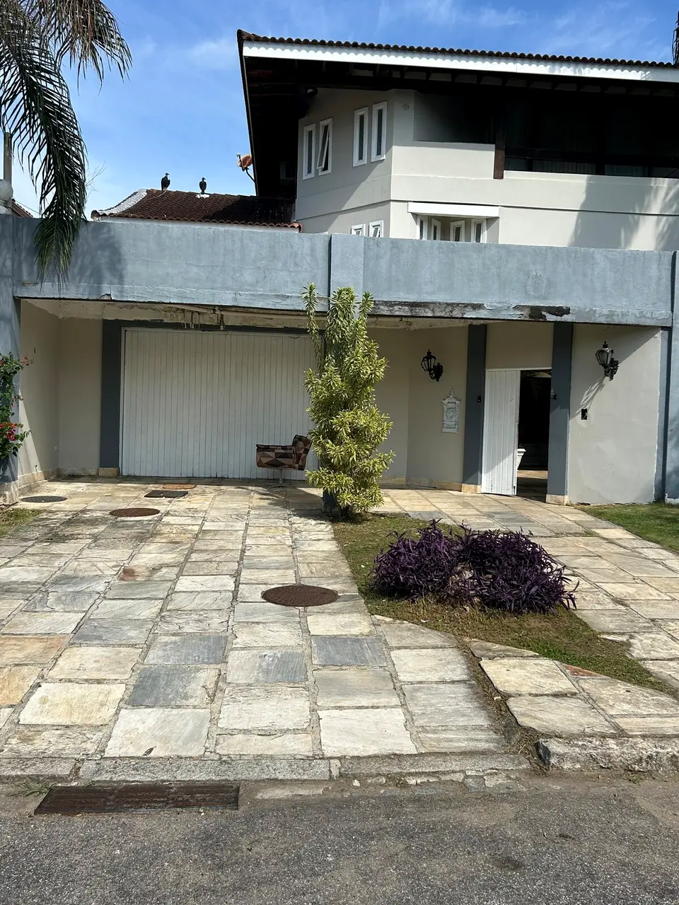 Fachada de entrada da mansão com garagem, portão e jardim, sob céu azul