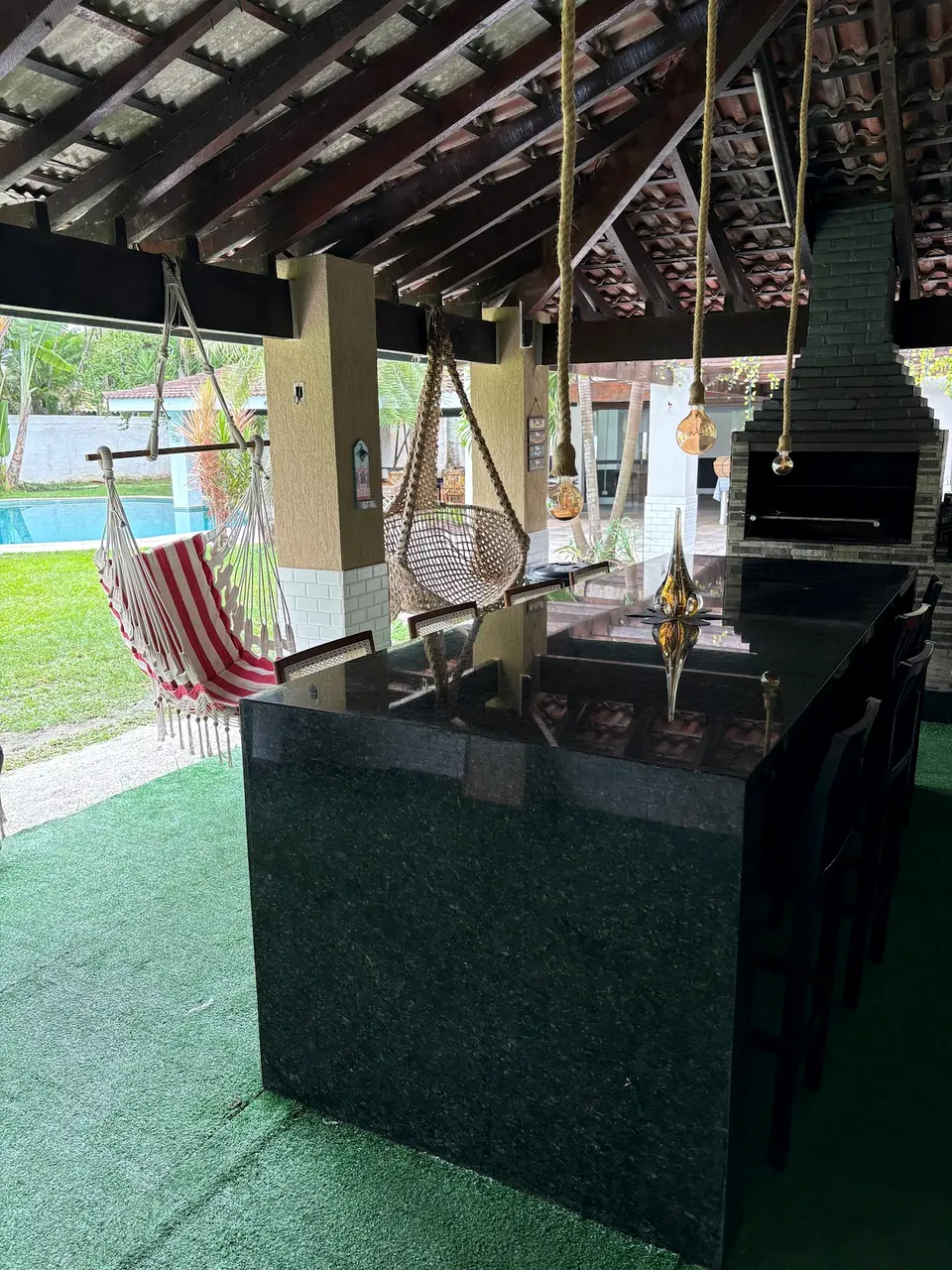 Bancada de granito preto do espaço gourmet, com banquetas e iluminação pendente