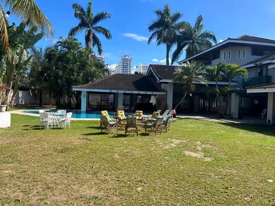 Vista do jardim e da piscina da mansão, com pavilhão de telha colonial e coqueiros ao fundo, em dia de céu azul