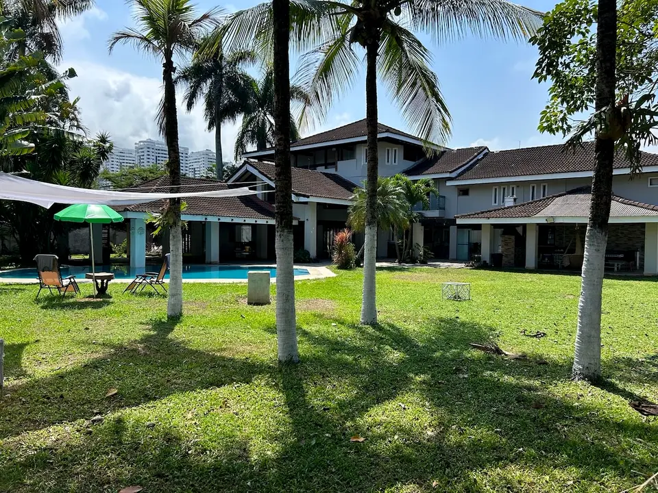Fachada dos fundos da mansão vista do jardim, entre coqueiros, com a piscina em primeiro plano