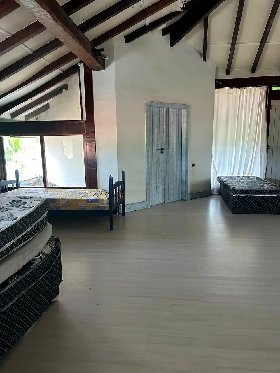 Quarto 4 da mansão, amplo, com múltiplas camas de casal e de solteiro sob telhado com estrutura de madeira aparente